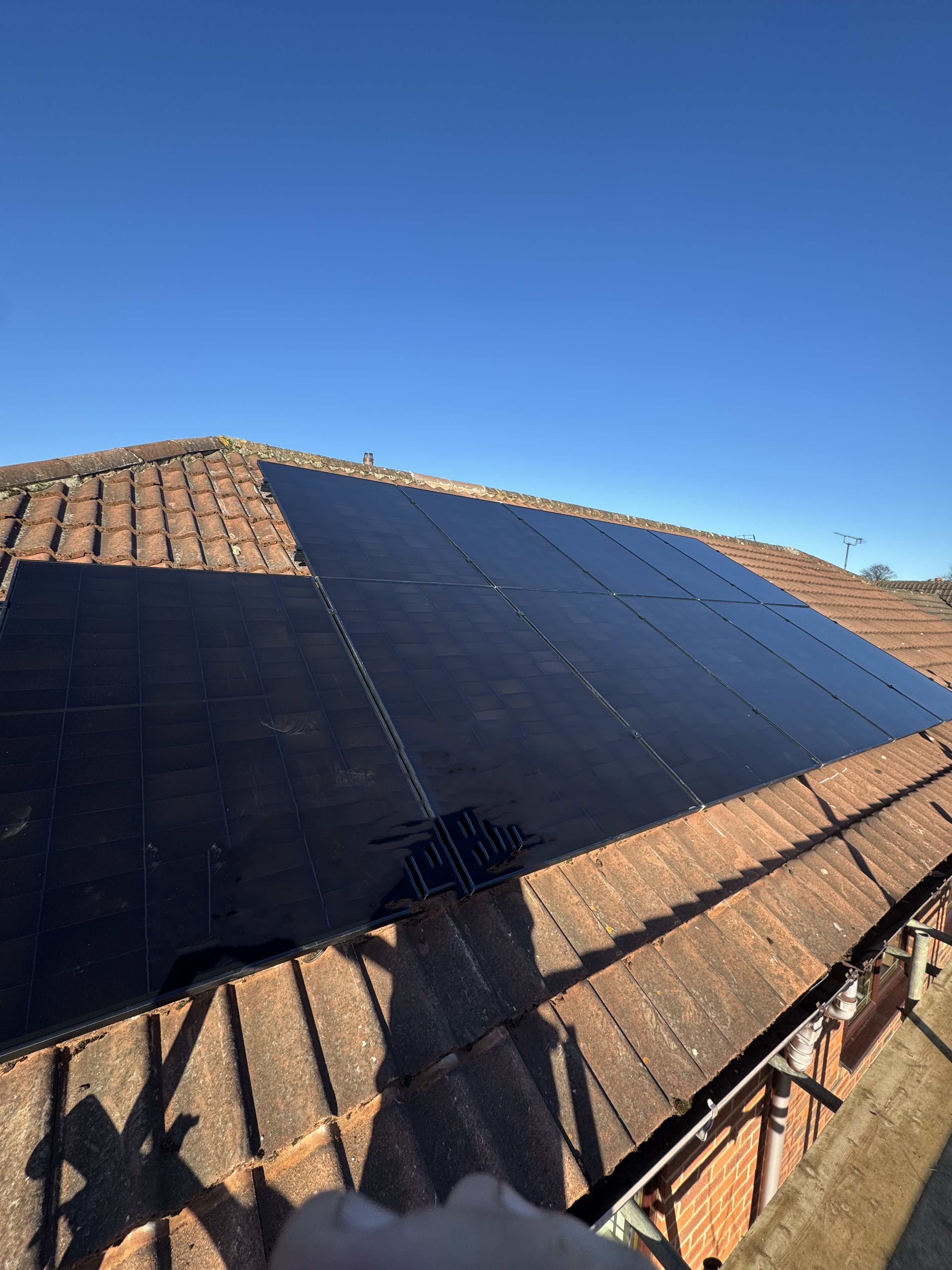 Black on black solar panels situated on a pitched roof on a sunny day.
