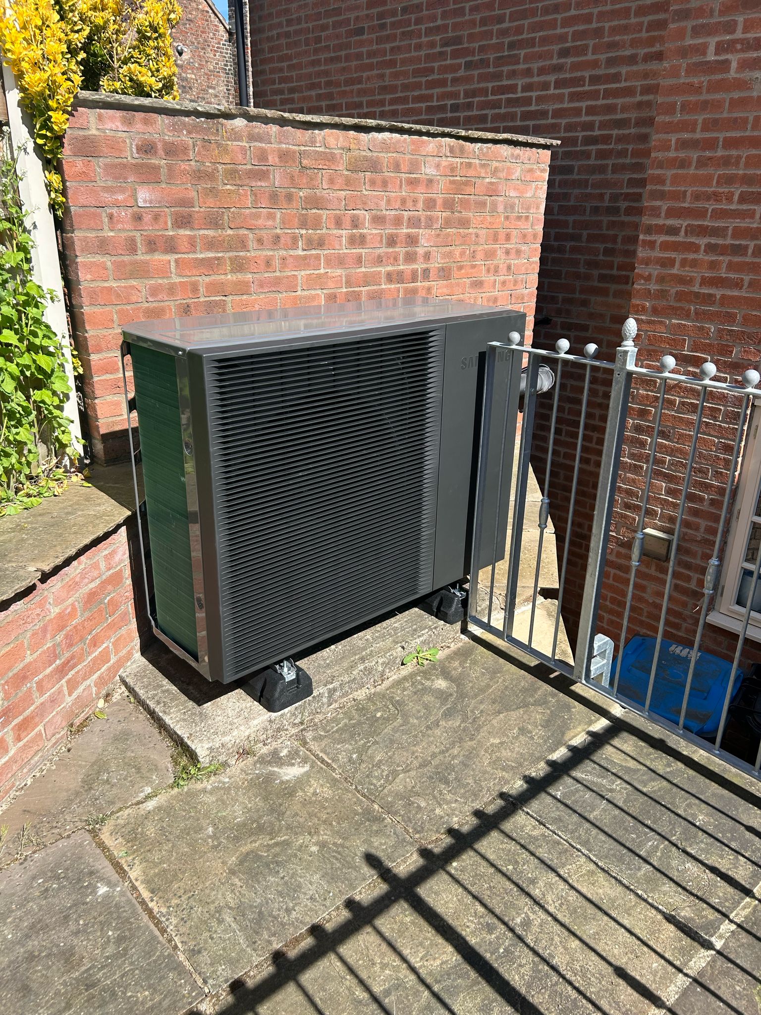 A Samsung air source heat pump fan installed outside a home at the top of some steps.